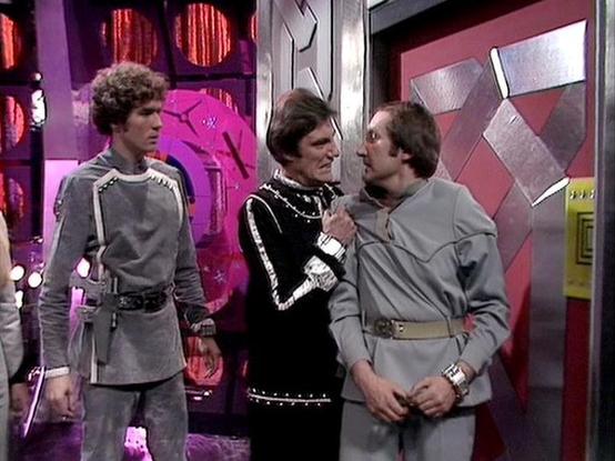 Claude Sonnet 4.0 describes the image as: "This scene takes place in what appears to be a futuristic spacecraft or space station interior, characterized by the distinctive metallic walls and technological panels typical of the series' production design. The setting has a sterile, high-tech aesthetic with geometric patterns and industrial lighting.

In the scene, three characters are positioned in what appears to be a corridor or operational area. One figure stands to the left observing the inte…