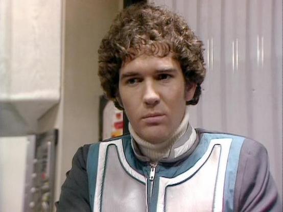 Claude Sonnet 4.0 describes the image as: "I can see this appears to be from a science fiction television series, showing someone in what looks like a futuristic white and blue uniform or flight suit. The setting appears to be inside a spacecraft or space station, with white paneled walls and what seems to be technical equipment visible in the background. The costume design has a distinctive retro-futuristic aesthetic typical of British science fiction from that era, with clean lines and a coll…