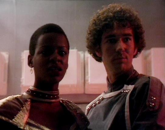 Claude Sonnet 4.0 describes the image as: "I can see two people in what appears to be a science fiction setting with futuristic costumes and lighting. However, I cannot identify who these specific individuals are based on their appearance alone. The scene appears to be from a television production, with dramatic lighting and what looks like a spacecraft or futuristic interior setting in the background. The costumes and production design suggest this is from a science fiction series, with the ch…