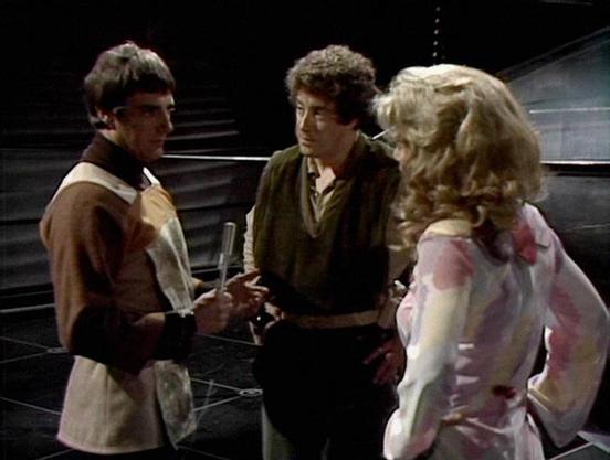 Claude Sonnet 4.0 describes the image as: "This scene appears to be set on a spaceship or space station, with metallic corridors and industrial-style architecture visible in the background. The lighting creates a dramatic, somewhat tense atmosphere typical of science fiction television. Three characters are engaged in what seems to be an important conversation or confrontation. One figure wears earth-toned clothing, another is in darker attire, and the third character has blonde hair and is wea…