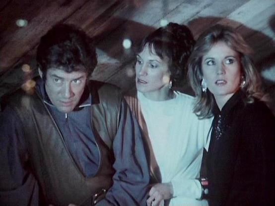Claude 3.7 describes the image as: "This image appears to be from a science fiction television series from the late 1970s or early 1980s, showing three individuals in what seems to be a dimly lit spacecraft or futuristic setting. The lighting has a bluish tint giving the scene a tense, dramatic atmosphere. 

On the left is a person wearing dark clothing with a serious expression. In the middle is someone with dark hair styled up, wearing a white or light-colored top. On the right is a person wi…