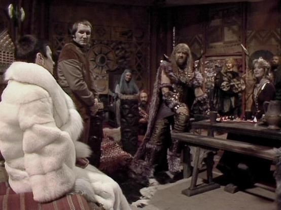 Claude Sonnet 4.0 describes the image as: "This scene appears to be set in a rustic, medieval-style interior with wooden furnishings and stone walls. The setting has a tavern or inn-like atmosphere with various characters gathered around. The lighting is dim and atmospheric, creating a sense of intrigue or clandestine meeting.

The characters are dressed in period costumes that suggest this is either a historical setting or perhaps the crew is in disguise. There's a mix of clothing styles, from…