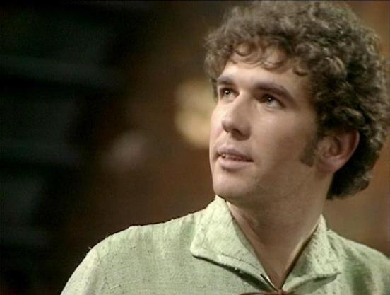 Claude 3.7 describes the image as: "The image shows a scene from what appears to be a vintage television production, likely from the late 1970s or early 1980s based on the filming style and aesthetic. 

The person in the frame has curly hair and is wearing a light-colored collared shirt or jacket. Their expression suggests they're engaged in conversation or reacting to something happening in the scene. 

The background is somewhat dark and blurred, which is characteristic of studio filming tech…