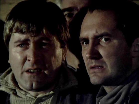 Claude 3.7 describes the image as: "This appears to be a still from a dramatic scene in what looks like a science fiction television production from the late 1970s or early 1980s, based on the film quality and visual style. 

The image shows two individuals in what seems to be a tense moment. The person on the left wears a light-colored garment with a collar, while the person on the right is in darker clothing. Both have concerned or alarmed expressions on their faces, suggesting they may be re…