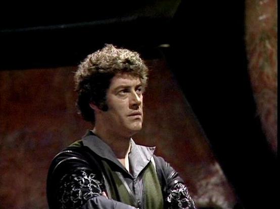 Claude Sonnet 4.0 describes the image as: "I can see this appears to be from a science fiction television production, showing someone in what looks like a futuristic or period costume with ornate details and embroidery. The setting appears to be indoors with reddish-brown walls or surfaces visible in the background. The lighting and image quality suggest this is from an older television production, likely from the late 1970s or early 1980s era. The costume design has a theatrical quality typica…