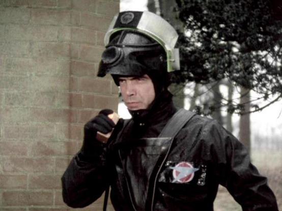 Claude Sonnet 4.0 describes the image as: "I can see this image shows someone in a dark uniform with protective gear including a helmet with a visor. They're wearing what appears to be a federation or military-style outfit with patches or insignia. The setting looks like it's near a brick building with some foliage visible in the background, suggesting an outdoor scene. The uniform and equipment suggest this is likely a security or military personnel character from a science fiction setting. Ho…