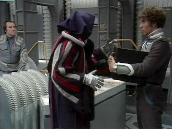 Claude 3.7 describes the image as: "This image shows a scene from a science fiction television series, set in what appears to be a spacecraft or space station interior. The setting features metallic walls and control panels typical of retro sci-fi production design.

The scene includes three figures: two people in standard clothing appropriate for the show's futuristic setting, and between them is a distinctive alien or masked character wearing a dark purple/blue outfit with red and white accen…