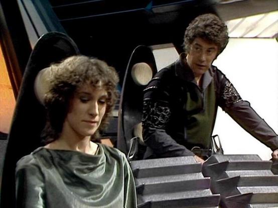Claude Sonnet 4.0 describes the image as: "This scene appears to be set aboard a spacecraft, likely the Liberator, showing the ship's sleek, futuristic interior with characteristic lighting and control surfaces. The setting has the distinctive aesthetic of the series - clean lines, metallic surfaces, and ambient lighting that creates dramatic shadows. Two characters are positioned at what appears to be a control station or bridge area. One character is seated at the controls while another stand…