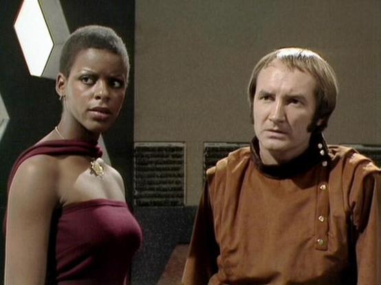 Claude 3.7 describes the image as: "The image shows a scene from a science fiction television series, featuring two characters in a futuristic setting. On the left is a person wearing a burgundy outfit with an off-shoulder design and a decorative brooch or insignia. On the right is someone in a brown/tan uniform with distinctive fasteners. The scene appears to be taking place in what looks like a spacecraft or space station interior, with technical panels visible in the background.

The styling…
