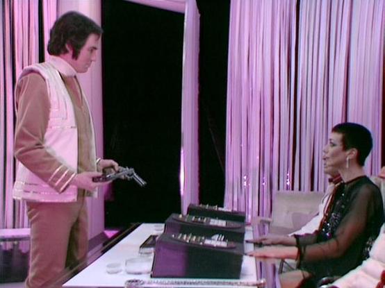 Claude 3.7 describes the image as: "The image shows a dramatic scene set in what appears to be a futuristic control room or office with striking pink/purple lighting and curtain-like vertical stripes in the background. 

On the left stands a person wearing a light-colored jacket with some detailing on the sleeves, holding what looks like a gun or weapon. On the right, seated at what appears to be a control console with various technological elements, is another person in dark clothing with shor…