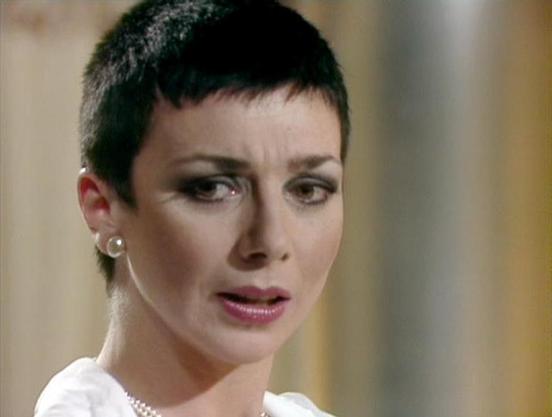 Claude Sonnet 4.0 describes the image as: "I can see this is an image from a television production featuring a person with very short dark hair and dramatic makeup, including dark eye makeup and lipstick. They're wearing what appears to be a white garment with pearl details around the neckline. The lighting and production values suggest this is from a science fiction television series, likely from the late 1970s or early 1980s based on the visual style. The setting appears to be indoors with so…