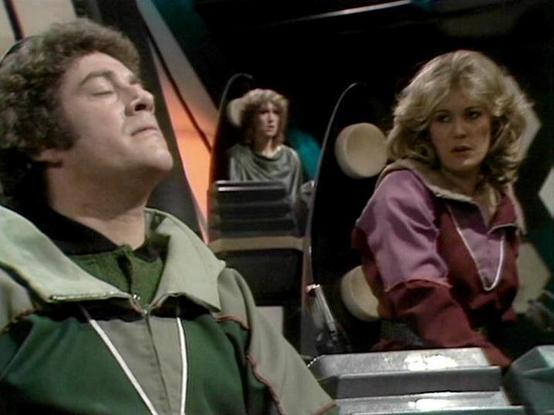 Claude Sonnet 4.0 describes the image as: "This appears to be a scene set aboard a spacecraft, likely the Liberator, showing three crew members in what looks like the flight deck or control area. The setting has the characteristic futuristic interior design with curved walls and technological elements typical of the series. One person is wearing a green outfit and appears to be resting or unconscious, while another crew member in reddish/purple clothing looks on with concern. A third figure can…