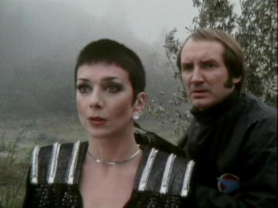 Claude Sonnet 4.0 describes the image as: "I can see this appears to be from a science fiction television series, showing two characters in what looks like an outdoor, misty or foggy setting with trees visible in the background. One character has very short dark hair and is wearing what appears to be a metallic or reflective costume with vertical striping. The other character has longer hair and is wearing dark clothing. The atmospheric, overcast setting and costume design suggest this is from …