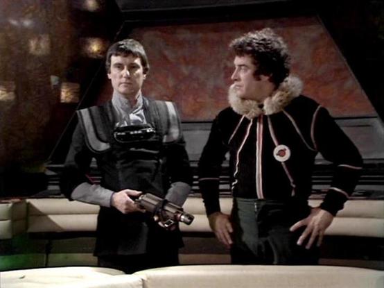 Claude Sonnet 4.0 describes the image as: "This scene shows two characters in what appears to be the interior of a spacecraft, likely the Liberator. The setting has a distinctive futuristic design with curved walls and lighting typical of the show's aesthetic. One character wears dark leather-style clothing and holds what appears to be a weapon, while the other is dressed in a black outfit with fur trim around the collar. They appear to be having a conversation while seated on what looks like a…