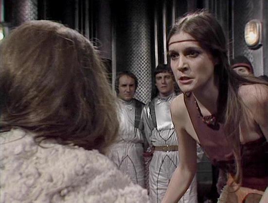 Claude Sonnet 4.0 describes the image as: "This appears to be a scene set in what looks like a spaceship or futuristic facility, with metallic corridors and industrial lighting visible in the background. The scene shows several characters in period-appropriate costumes - some wearing light-colored, loose-fitting garments while others are in darker clothing. The setting has the distinctive production design typical of late 1970s science fiction television, with practical lighting effects and cor…
