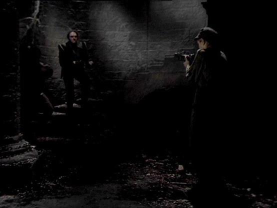 Claude Sonnet 4.0 describes the image as: "I can see this is a dark, atmospheric scene set in what appears to be an underground or dungeon-like environment with stone walls. The lighting is dim and moody, creating shadows throughout the space. There are figures visible in the scene - some standing and positioned in different areas of this stone chamber or corridor. The setting has a gritty, oppressive feel typical of a prison or underground facility. The stone architecture and low lighting cont…