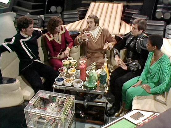 Claude Sonnet 4.0 describes the image as: "This scene shows the crew gathered in what appears to be a luxurious lounge area aboard their ship. The setting features comfortable seating arranged around an elegant glass coffee table laden with refreshments including drinks, snacks, and what looks like tea service. The space has a sophisticated, almost decadent atmosphere with rich furnishings and warm lighting.

The crew members are dressed in their typical attire - some in leather jackets and oth…