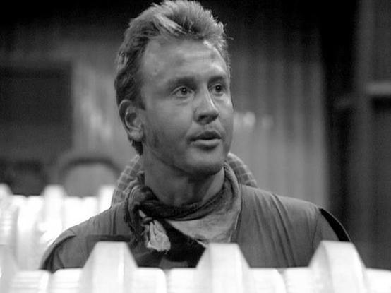 Claude 3.7 describes the image as: "This is a black and white image from a television scene. The frame shows a person wearing what appears to be a utilitarian jacket or vest with a scarf or bandana around their neck. The individual has a somewhat surprised or concerned expression and appears to be in what might be a spacecraft or futuristic setting, which is characteristic of science fiction productions from the late 1970s or early 1980s.

The composition shows the person from chest up, with so…