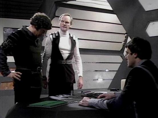 Claude Sonnet 4.0 describes the image as: "I can see this appears to be from a science fiction television series, showing three people in what looks like a futuristic spacecraft or station interior. The setting has characteristic sci-fi design elements including curved walls with horizontal ribbing and control panels with various displays and controls. One person is wearing what appears to be a light-colored uniform or outfit, while the others are in darker clothing. They appear to be engaged i…