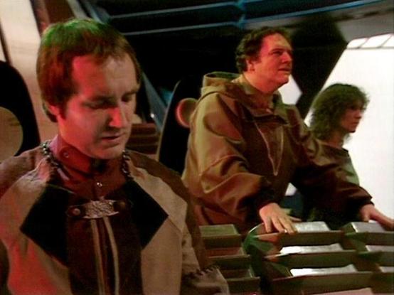 Claude Sonnet 4.0 describes the image as: "I can see this appears to be a scene from inside a spacecraft or futuristic setting, with what looks like a control room or bridge environment. The lighting has a distinctive colored tint that was characteristic of sci-fi productions from that era. There are several people in the scene wearing what appears to be period-appropriate costume design, but I cannot identify specific individuals in the image. The setting suggests this is likely from a dramati…