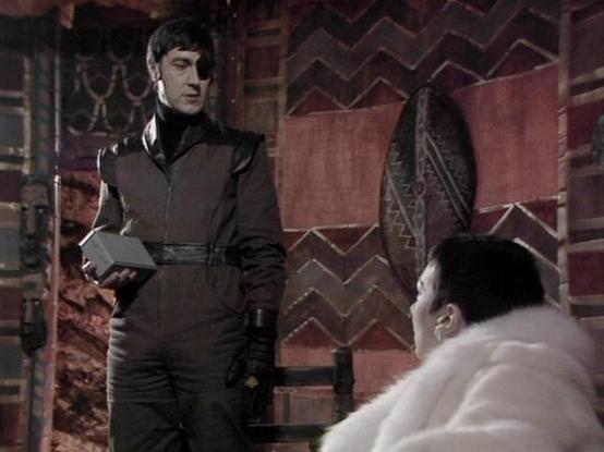 Claude Sonnet 4.0 describes the image as: "I can see this is a scene with two characters in what appears to be an ornate, futuristic setting with decorative brick or tiled walls featuring geometric patterns. One figure is wearing a dark military-style uniform and appears to be standing in a position of authority, while another character in lighter colored clothing is seated or reclining. The setting has an elaborate, imperial aesthetic typical of the show's design, with rich textures and archit…