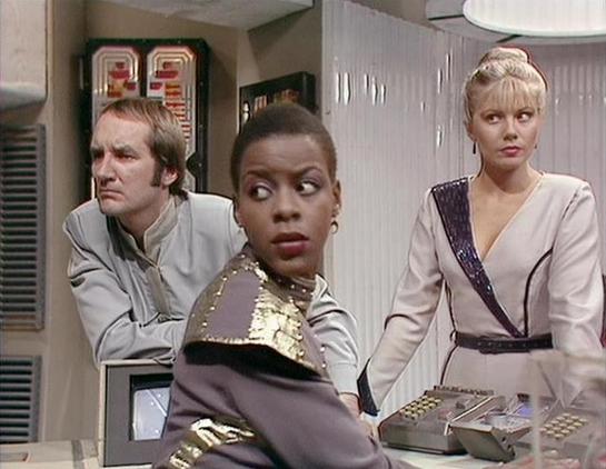 Claude Sonnet 4.0 describes the image as: "This scene appears to be set aboard a spacecraft, likely the Liberator or Scorpio, showing the ship's control room or flight deck. The futuristic interior features white walls, control panels, and technical equipment typical of the series' design aesthetic. Three crew members are present - one wearing a light-colored uniform standing in the background, another in the center wearing what appears to be a metallic or leather outfit with decorative studs, …