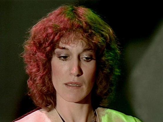 Claude Sonnet 4.0 describes the image as: "I can see this appears to be from a science fiction television production, likely from the late 1970s or early 1980s based on the visual style and lighting effects. The image shows a person with distinctively styled curly hair that has been colored with red and green highlights or lighting effects, creating an otherworldly appearance. They're wearing what appears to be a light-colored garment and a necklace. The dramatic colored lighting - particularly…