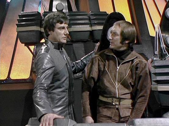 Claude Sonnet 4.0 describes the image as: "This scene shows two crew members aboard the Liberator spacecraft. One character wears a distinctive black leather outfit with studded details, while the other is dressed in brown leather. They appear to be having an intense conversation in what looks like the ship's flight deck or control area, with the characteristic curved walls and technical equipment visible in the background. The futuristic set design features the show's typical metallic and angu…