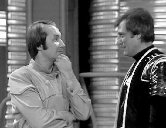 Claude Sonnet 4.0 describes the image as: "I can see this is a black and white photograph showing two men in what appears to be an indoor setting with venetian blinds visible in the background. One man is wearing a light-colored casual shirt and has his hand thoughtfully positioned near his chin, while the other is dressed in what looks like a dark formal jacket or uniform with decorative elements. The lighting creates dramatic shadows through the blinds, giving the scene a film noir quality. T…
