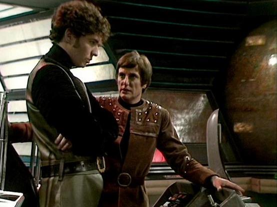 Claude Sonnet 4.0 describes the image as: "I can see two men in what appears to be a futuristic spacecraft interior with metallic walls and control panels. One man is wearing a dark jacket or vest, while the other is dressed in a brown leather outfit with decorative studs or details. They appear to be having a conversation in what looks like the ship's control room or bridge area. The setting has the distinctive retro-futuristic aesthetic typical of late 1970s science fiction television, with c…