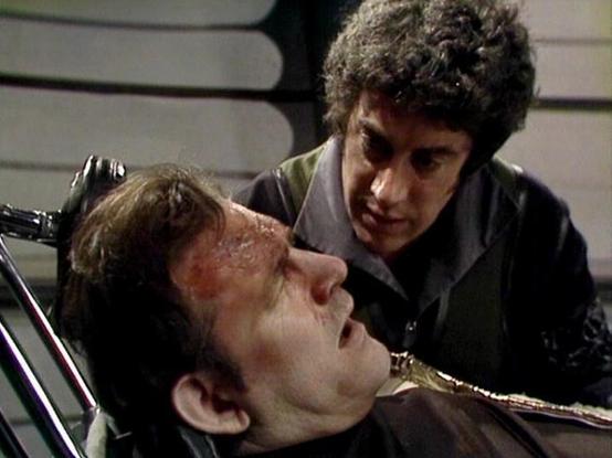 Claude Sonnet 4.0 describes the image as: "I can see this is a dramatic scene showing two characters in what appears to be a tense, intimate moment. One man is lying down or reclining, appearing injured or distressed, while another man with dark curly hair leans over him in what seems to be either a threatening or concerned gesture. The setting appears to be inside a spacecraft or futuristic facility, with sleek, metallic surfaces visible in the background. The lighting and composition create a…