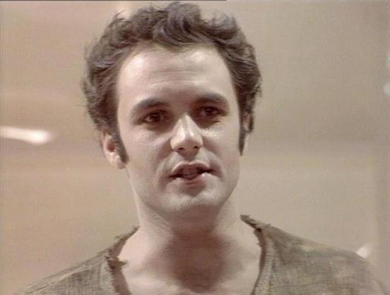 Claude Sonnet 4.0 describes the image as: "I can see this appears to be from a science fiction television production, showing a man with curly dark hair wearing what looks like a light-colored or beige garment. The setting appears to be indoors with neutral-toned walls or surfaces in the background. The lighting and image quality suggest this is from a television production from several decades ago. The person appears to be in some kind of scene or dialogue moment. However, I cannot identify wh…
