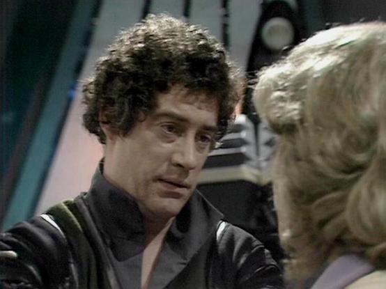 Claude Sonnet 4.0 describes the image as: "I can see this appears to be from a science fiction television series, showing what looks like a scene between two characters in what appears to be a spacecraft or futuristic setting. The image shows a man with dark curly hair wearing what appears to be a dark colored outfit, and there's a blonde woman visible in the frame. The setting has the typical aesthetic of 1970s/80s science fiction television production, with what looks like technological equip…