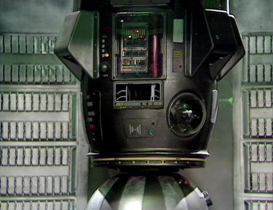 Claude Sonnet 4.0 describes the image as: "This image shows the interior of a spacecraft, featuring a distinctive control console or computer terminal with various screens, displays, and control panels. The setting has a futuristic, sterile appearance with white/grey paneled walls typical of science fiction production design from the late 1970s. The console features multiple monitors, indicator lights, and what appears to be a circular viewing port or scanner. The technical equipment has a util…