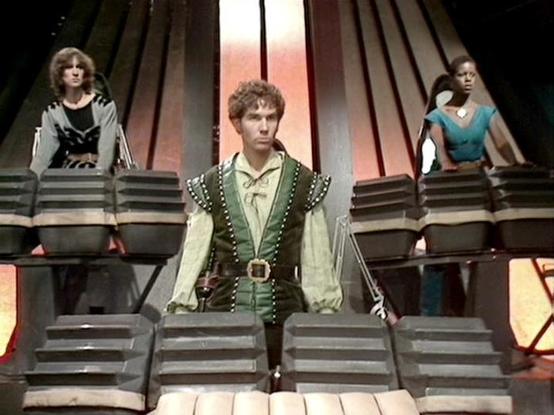 Claude Sonnet 4.0 describes the image as: "This appears to be a scene set aboard a spacecraft, featuring three characters positioned on what looks like a multi-level bridge or control room set. The central figure wears a distinctive green and cream medieval-style tunic with studded leather details, standing prominently on steps or a raised platform. Two other characters are positioned on either side at different levels - one wearing dark clothing on the left, and another in a teal/blue outfit o…