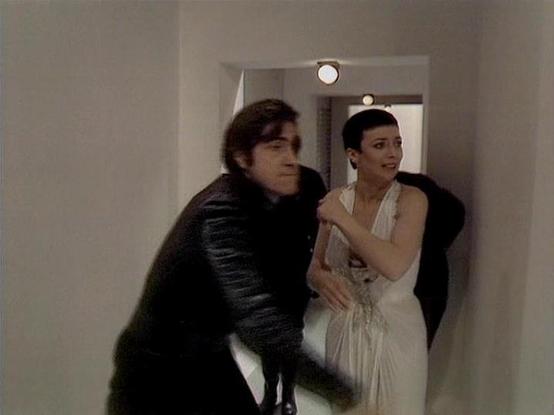 Claude 3.7 describes the image as: "This image appears to be from a television series, showing two people in what looks like a hallway or corridor with white walls. The scene features someone wearing a dark outfit or jacket on the left, while the person on the right is wearing a white or light-colored dress or gown. They appear to be in some kind of dramatic moment or confrontation within what seems to be a futuristic or institutional setting, based on the minimalist design of the background. T…