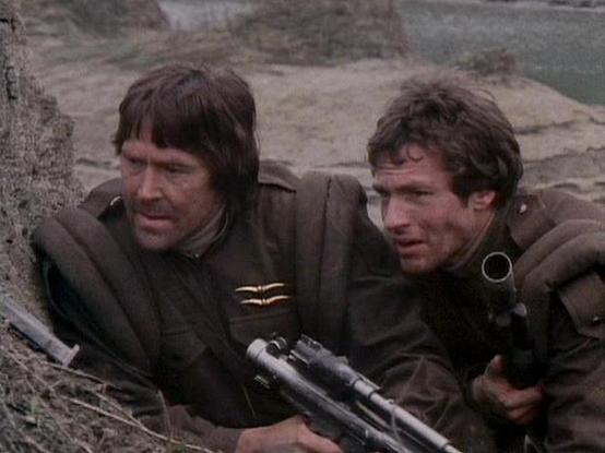 Claude 3.7 describes the image as: "The image shows two people in what appears to be a battle or survival scenario, taking cover behind what looks like rocky terrain. They're wearing dark brown military-style jackets or uniforms and appear to be armed with weapons. The setting has a gritty, desaturated color palette typical of older science fiction productions, with a barren landscape visible in the background.

The scene appears to be from a dramatic moment where the characters are in a tense …