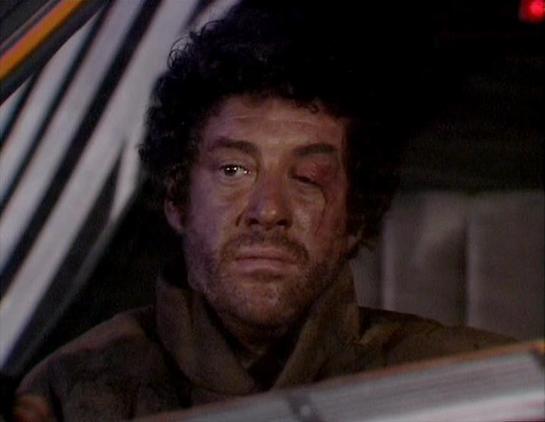 Claude Sonnet 4.0 describes the image as: "I can see this appears to be from a science fiction television series, showing someone in what looks like a vehicle or spacecraft interior. The person appears injured or distressed, with visible bruising or marks on their face. They're wearing what appears to be dark clothing, and the lighting and set design has the characteristic look of 1970s British television production. The interior setting suggests this might be from a dramatic or action sequence…