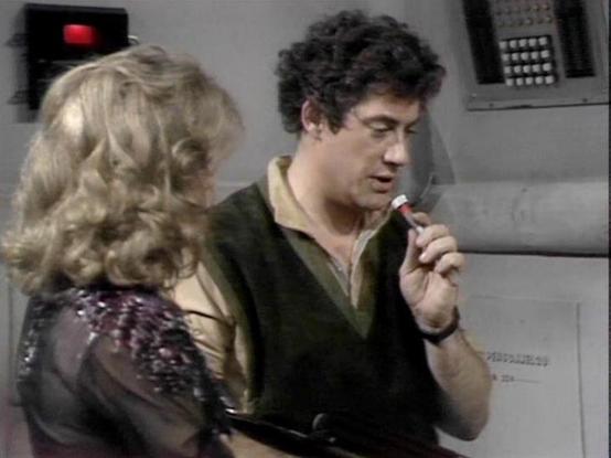 Claude Sonnet 4.0 describes the image as: "I can see this appears to be from a science fiction television series, showing two people in what looks like a futuristic spacecraft or space station setting. The environment has the characteristic utilitarian, high-tech aesthetic typical of sci-fi productions from that era, with control panels and metallic surfaces visible in the background.

One person has curly blonde hair and is wearing what appears to be a dark, sequined or textured outfit. The ot…