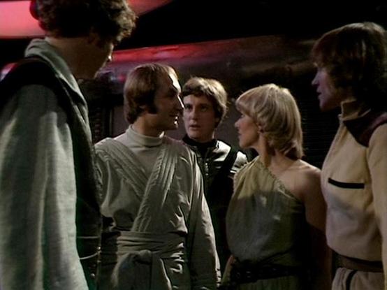 Claude Sonnet 4.0 describes the image as: "This appears to be a scene set aboard a spacecraft, likely the Liberator, with several crew members gathered in what looks like the ship's corridor or common area. The lighting has the characteristic dim, atmospheric quality typical of the series' interior shots. The characters are wearing their usual practical space-faring attire - neutral-colored clothing suitable for life aboard a rebel ship. The group appears to be engaged in discussion, possibly p…
