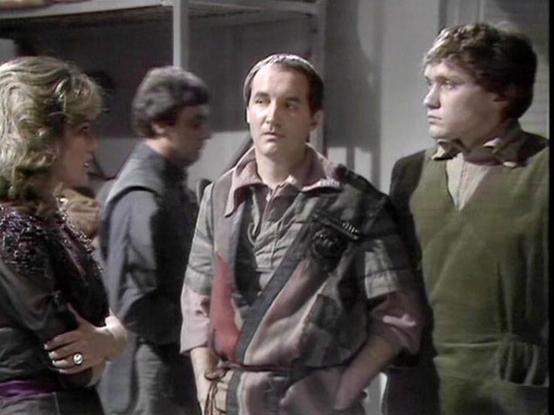 Claude Sonnet 4.0 describes the image as: "This appears to be a scene set in what looks like a spacecraft or futuristic facility interior, with metallic walls and institutional lighting typical of science fiction productions from this era. The scene shows several characters in conversation, with costumes reflecting the show's distinctive late 1970s sci-fi aesthetic. The characters are wearing a mix of practical spacefaring garments and more elaborate period-appropriate clothing. The lighting an…