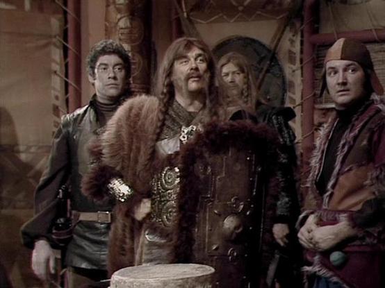 Claude Sonnet 4.0 describes the image as: "This appears to be a scene set in what looks like a medieval or fantasy-themed environment, with stone archways and rustic architecture visible in the background. The characters are dressed in period costumes including leather, fur trim, and ornate medieval-style clothing with decorative elements. The setting suggests this might be taking place in a castle, tavern, or similar historical location. The lighting and overall aesthetic give it a dramatic, a…
