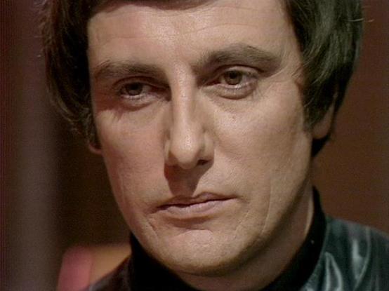 Claude Sonnet 4.0 describes the image as: "I can see this is a close-up shot of a man with dark hair and intense eyes, appearing to be in dramatic lighting typical of science fiction television from the late 1970s or early 1980s. The image has the distinctive look and production quality characteristic of British sci-fi television from that era. The lighting and cinematography create a moody, serious atmosphere. However, I cannot identify who this specific actor is based on their appearance alon…