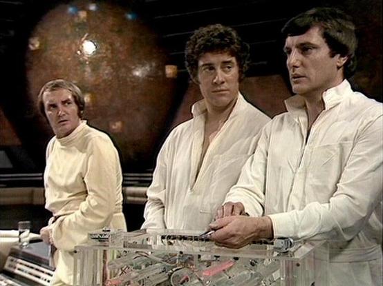 Claude Sonnet 4.0 describes the image as: "This scene appears to be set on a spacecraft bridge or control room, with three crew members dressed in white uniforms gathered around what looks like a control console or tactical display. The futuristic setting features a large spherical object visible in the background, suggesting they may be viewing a planet or space station. The lighting and set design have the distinctive look of late 1970s British science fiction television, with metallic surfac…
