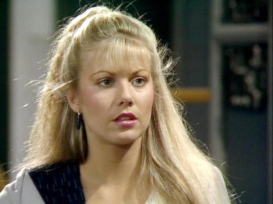 Claude Sonnet 4.0 describes the image as: "I can see this is an image of a blonde woman with long hair styled with bangs, wearing what appears to be a dark vest or sleeveless top. The setting looks like it could be from a science fiction production, with blurred architectural elements in the background. The lighting and image quality suggest this is from a television production, likely from the 1980s based on the styling and film quality. The woman has an intense, focused expression and appears…