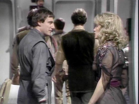 Claude Sonnet 4.0 describes the image as: "This appears to be a scene set aboard a spacecraft, likely the Liberator, with its characteristic sterile, futuristic interior visible in the background. The setting shows what appears to be a corridor or common area of the ship. Multiple crew members are present in the scene, wearing the typical earth-toned, practical clothing characteristic of the series. The lighting and production values are typical of late 1970s British science fiction television.…