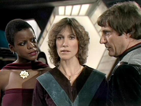 Claude Sonnet 4.0 describes the image as: "This scene appears to be set aboard a spacecraft, likely the Liberator, given the futuristic interior visible in the background. The three characters are positioned close together in what seems to be an intense moment of conversation or decision-making. The setting has the characteristic clean, technological aesthetic typical of the series, with curved walls and lighting that suggests an advanced spaceship environment. The characters appear to be engag…