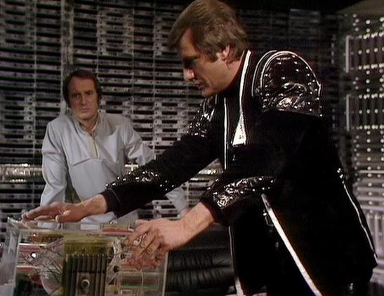 Claude Sonnet 4.0 describes the image as: "I can see this is a scene set in what appears to be a futuristic control room or technical facility, with characteristic sci-fi styling including metallic surfaces and electronic equipment in the background. Two characters are present - one wearing light-colored clothing in the background, and another in the foreground wearing a distinctive black leather outfit with decorative studs or embellishments. The character in black appears to be operating or e…
