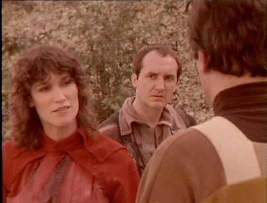 Claude Sonnet 4.0 describes the image as: "I can see this appears to be from a science fiction television production, showing three people in what looks like an outdoor setting with a textured wall or rocky surface in the background. The scene has the characteristic visual style of late 1970s/early 1980s television drama. One person is wearing a distinctive red/burgundy colored outfit, while another is in more muted tones. The lighting and film quality suggest this is from a dramatic scene, pos…