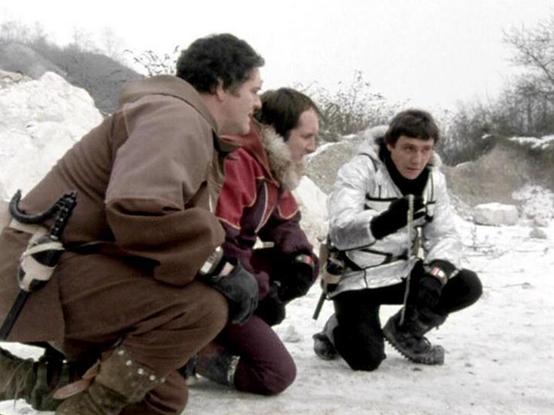 Claude Sonnet 4.0 describes the image as: "I can see three people in winter/cold weather gear kneeling in what appears to be a snowy, rocky terrain. They're wearing heavy coats and appear to be in some kind of outdoor survival or mission scenario. The setting looks harsh and desolate, with white rocky formations or snow-covered ground visible in the background. The individuals appear to be taking shelter or regrouping in this challenging environment. The scene has the look of a science fiction …